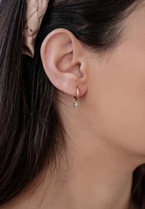 Goldene Creolen mit einem kleinen klaren, diamantförmigen Akzent. Einfaches Design, glatte Textur und kompakte Form.