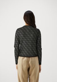 Pull en maille noire avec un motif en diamant, manches longues et col rond. Bas et poignets côtelés. Porté par-dessus un pantalon beige.