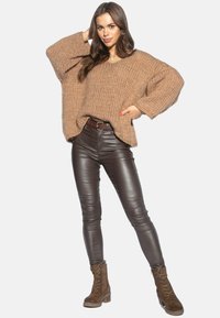 Przesadzony brązowy sweter dzianinowy z dekoltem w serek, zestawiony z eleganckimi brązowymi skórzanymi spodniami oraz brązowymi za costami za kostkę.