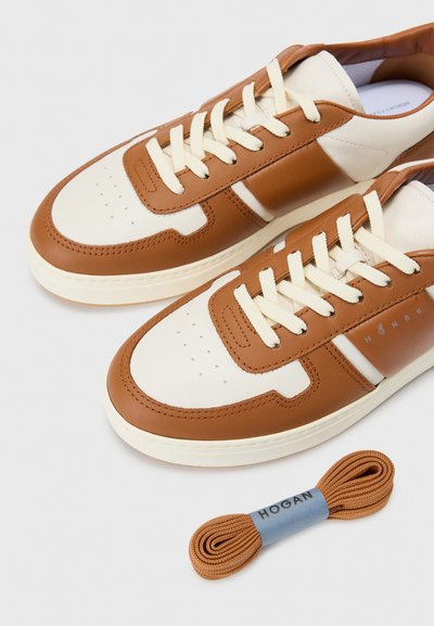 Lace-up sneakers med en ovandel i krämfärgad och tan läder, perforerad tå och en kontrasterande tan-rand. Inkluderar ett extra par bruna snören.