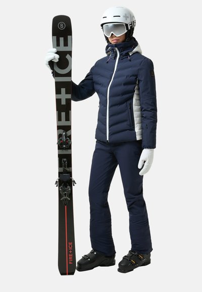 Navy and white padded ski jacket paired with navy ski pants, white gloves, and black skis featuring red accents and bindings.