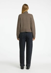 Brauner Strickpullover mit Rollkragen und verkürztem Design, kombiniert mit hochgeschnittenen, dunkelblauen Jeans aus Denim mit umgeschlagenen Säumen und glatter Textur.