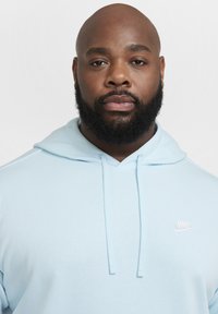 Felpa leggera blu chiaro realizzata in materiale morbido, con una tasca frontale e un piccolo logo Nike bianco sul petto. Stringhe regolabili sulla cappuccio.