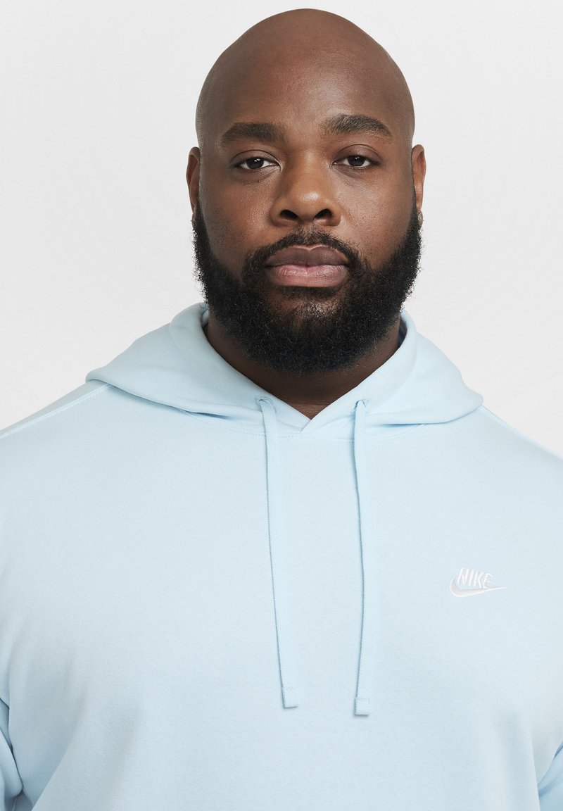 Sudadera azul claro hecha de material suave, con un bolsillo frontal y un pequeño logo blanco de Nike en el pecho. Cuerdas en la capucha.