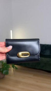 Black leather wallet featuring a rounded gold hardware clasp, smooth texture, and stitched edges. Compact design with no visible branding.