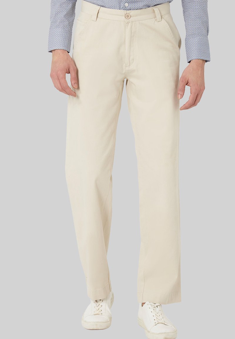 Pantalones de algodón beige con un diseño de pierna recta, que cuentan con cierre de botón, trabillas para cinturón y bolsillos laterales. Combinados con zapatillas blancas.