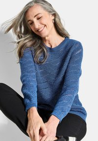 Blauer gestrickter Pullover mit strukturiertem Muster, Rundhalsausschnitt und langen Ärmeln. Kombiniert mit schwarzen Hosen.