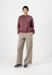 Burgundi värvi pusakorv, millel on väike logo, beežid laiad spordipüksid tekstiga ja sinised spordijalatsid. Tekstuur näeb välja pehme ja seljas mugav.