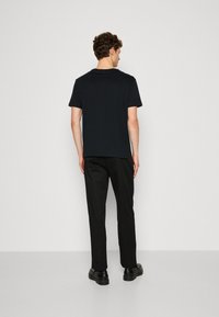 T-shirt noir en coton avec un col rond, des manches courtes et un ourlet droit, porté avec un pantalon noir et des chaussures noires. Vue arrière.