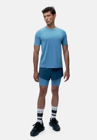 Maglietta atletica blu a maniche corte abbinata a pantaloni corti blu scuro. Sneakers nere e calze a righe completano l'outfit. Tessuto morbido, taglio moderno.