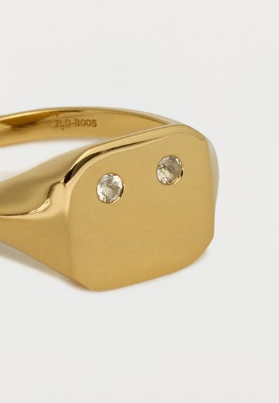 Χρυσό ορθογώνιο δαχτυλίδι με δύο μικρά στρογγυλά διαμάντια τοποθετημένα δίπλα δίπλα στην επίπεδη επιφάνεια.