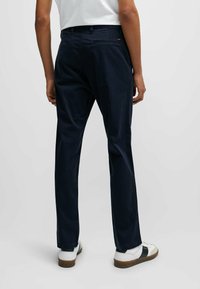 Navy cotton trousers with a straight fit, two back pockets, and a subtle brand tag. Worn with white shoes and a casual white top.