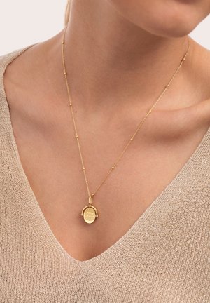 Collar de cadena dorada con pequeñas cuentas y un colgante redondo de oro grabado con "Mon Amour", llevado en el cuello de una persona sobre un top de punto beige.