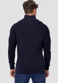 Navy nieprzylegający sweter z wysokim kołnierzem, długimi rękawami i teksturowanym wykończeniem, pokazany z tyłu na neutralnym tle.