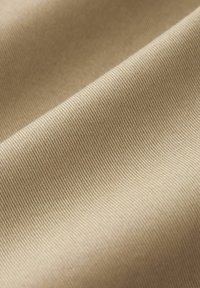 Beige stof close-up toont een glad, gestructureerd oppervlak met diagonale ribbels, dat het geweven patroon en de zachte glans benadrukt.