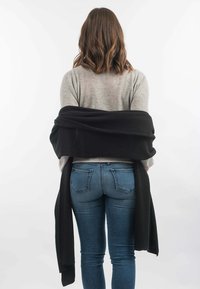 Sort indpakningssjal draperet over en lys grå sweater, med mellemblå skinny jeans. Glat tekstur, lange ender, minimalistisk design.
