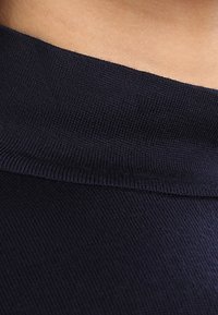 Marinblått stickat tyg med en mjuk textur, med en ribbad halsringning. Närbild som framhäver tygets stretch och väv.