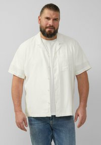 Biała koszula z krótkim rękawem, zapinana na guziki, z kieszonką, stworzona do noszenia na szarym t-shircie. Uzupełniona niebieskimi dżinsami. Miękka tekstura, luźny krój.