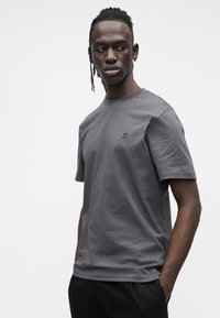 Szara bawełniana koszulka z krótkimi rękawami, o okrągłym dekolcie i małym haftowanym logo na piersi. Gładka tekstura i swobodny krój.