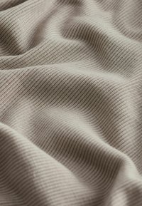 Texturiertes Rippgewebe in hellem Beige, mit sanften Wellen und subtiler Glanz, das die dehnbaren und fließenden Eigenschaften hervorhebt.
