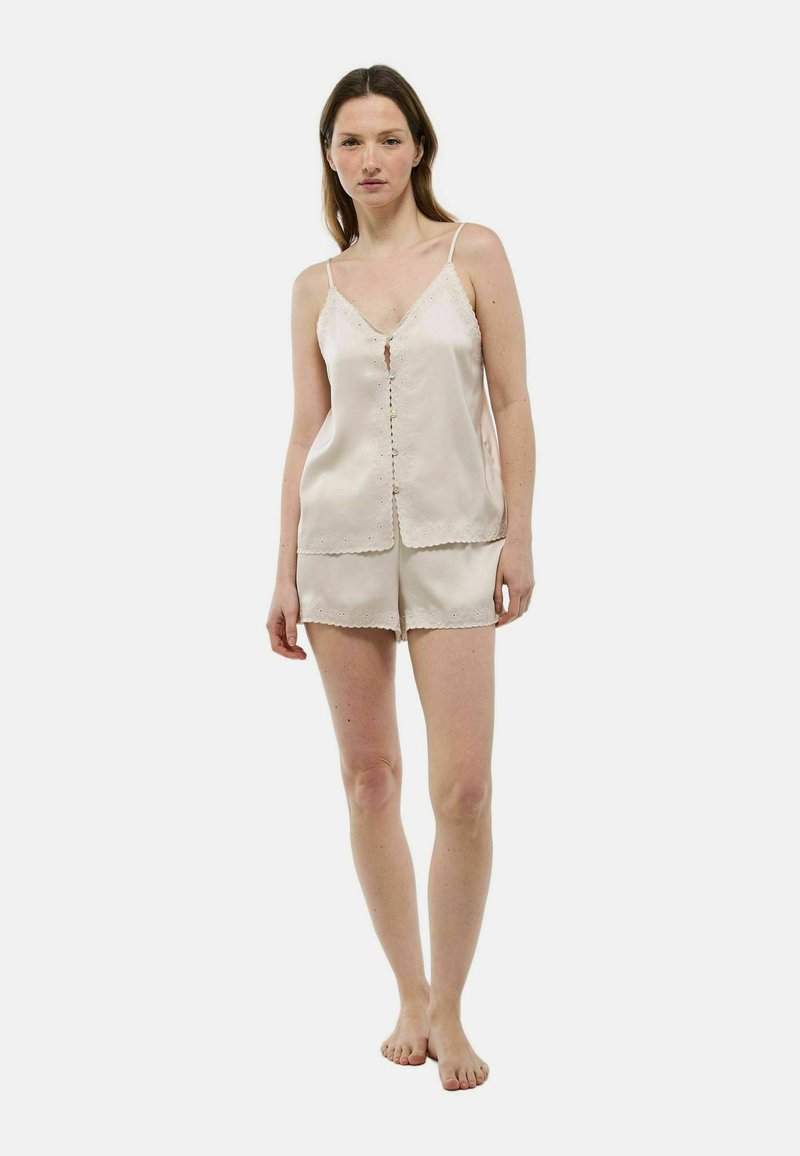 Ensemble de camisole et short en soie de couleur beige clair avec des garnitures en dentelle, comprenant des bretelles réglables et une fermeture à bouton sur le haut. Texture lisse.