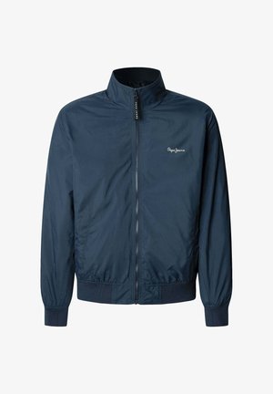 Mornarsko modra vetrovka iz lahkega materiala s pokončnim ovratnikom, sprednjim zadrgo ter elastičnimi manšetami in robom. Na prsih je logo.