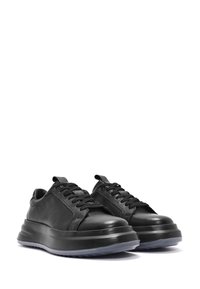 Sneakers in pelle nera con una suola intermedia nera spessa e superficie testurizzata. Presentano lacci rotondi e un occhiello per facilitare la calzata.