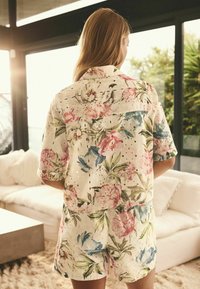 Blommig kortärmad skjorta och shorts-set med ögla detaljer, prydd med rosa och blå blommiga mönster på en vit bakgrund.