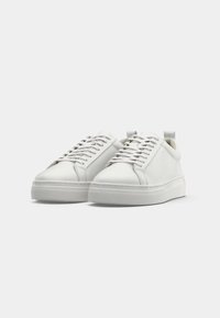Sneaker bianchi in pelle con punta arrotondata, lacci piatti, colletto imbottito e suola in gomma testurizzata; design minimalista e senza branding visibile.