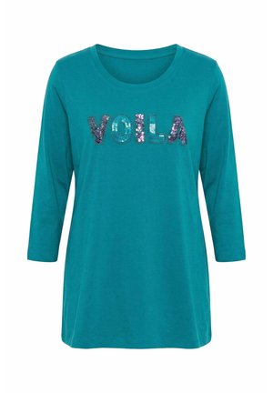 Morska zielona koszula z długim rękawem z okrągłym dekoltem, z napisem „VOILA” wykonanym z dużych, wielokolorowych cekinów na wysokości klatki piersiowej.