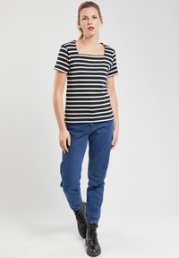 Haut à manches courtes noir et blanc à rayures avec un col carré, associé à un jean bleu et des bottes noires à lacets. Matière en coton lisse.