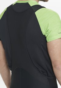 Schwarze Radsport-Bib-Shorts aus strukturiertem, dunklem Stoff und leuchtend grünen Kurzärmeln. Figurbetontes Design, atmungsaktives Mesh-Detail an den Schultern.