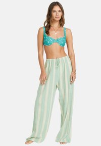 Haut de bikini à motif floral turquoise avec un pantalon de plage à larges rayures vertes, doté d'une taille à cordon, fabriqué en tissu léger.