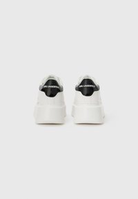 White sneakers with a chunky sole and black patent leather accents on the heel, featuring the "Karl Lagerfeld" logo in white text.