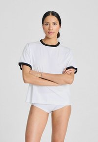 White T-shirt with black ribbed neckline and sleeve cuffs, featuring a relaxed fit. Model poses with arms crossed.