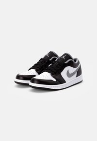 Zapatillas de cuero en blanco y negro con un diseño de corte bajo, caja de dedos perforada y acentos grises. Incluyen cordones negros y suela de goma.