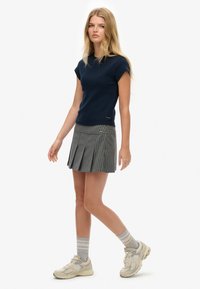 Navy blauw kortefblouse gecombineerd met een grijze gestreepte plooirok. Lichtgrijze sneakers en gemusterde sokken maken de look compleet.