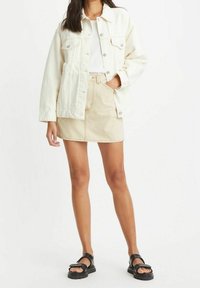 Bílá denimová bunda přes bílý top, doplněná béžovo-bílou pruhovanou mini sukní. Černé platformové sandály outfit dokončují.