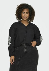 Cămașă neagră cu butoane, cu mâneci lungi, având motive decorative albe pe mâneci, asortată cu o fustă neagră din denim.