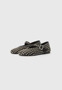 Chaussures plates noires avec un bout rond et une sangle avec une boucle, ornées de clous en argent couvrant la surface. Texture lisse.