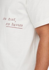 Weißes Baumwoll-T-Shirt mit rotem gesticktem Text "KEIN RISIKO, KEIN GEFÜHL" nahe der unteren linken Seite, mit kurzen Ärmeln und klassischer Passform.