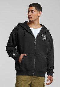 Sort zip-up hoodie lavet af bomuldsblanding med en frontlomme, ribbede manchetter og et broderet logo på brystet og ærmet.