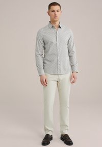 Camisa de botones en gris claro con un pequeño patrón geométrico, combinada con pantalones en color crema y mocasines oscuros. Tela suave y diseño ajustado.