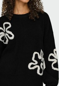 Zwarte gebreide trui met witte bloemmotieven. Beschikt over een ronde halslijn en lange mouwen, en biedt een textuurafwerking.