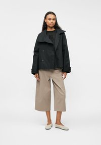 Abrigo negro tipo peacoat con botones de doble botonadura, amplios solapas, usado sobre una camiseta negra y culottes beige, combinado con zapatos de slip-on de color claro.