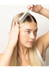 Pettine di plastica con manico beige, utilizzato su capelli dritti e biondi chiari; la mano dell'utente poggia sui capelli, con le unghie curate.