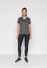 Maglietta sportiva nera mélange a scollo a V abbinata a leggings neri, caratterizzata da un tessuto traspirante e una finitura testurizzata. Scarpe da ginnastica nere.