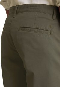 Pantalons vert olive avec poches arrière, une texture lisse et un branding subtil près de la taille. Design de taille plate pour le confort.