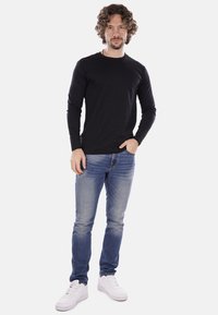 Camicetta nera a maniche lunghe abbinata a jeans blu sbiaditi e scarpe da ginnastica bianche. La camicia presenta un collo rotondo e un design aderente.