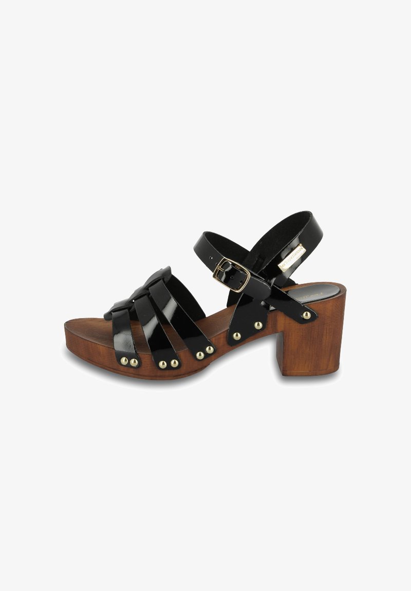 Sandalias de charol negro con un tacón de bloque de madera, que cuentan con múltiples correas cruzadas, tachuelas en tono dorado y un cierre de hebilla ajustable.